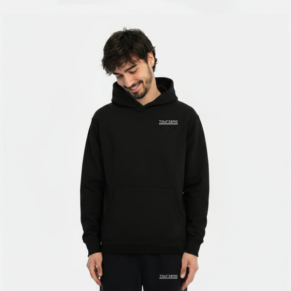 Homme souriant portant un hoodie noir TOURISMO et un pantalon assorti, regard vers le bas