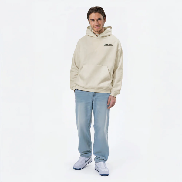 Homme souriant portant un hoodie beige TOURISMO avec un jean clair et des baskets blanches