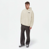 Homme debout en hoodie beige TOURISMO, pantalon foncé et baskets, style streetwear moderne et chic