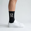 Chaussettes Ayrton Senna 12, saison 1988 noir, portées de profil avec des sneakers blanches