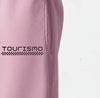 Gros plan sur le logo "Tourismo" blanc imprimé sur le pantalon de jogging rose.